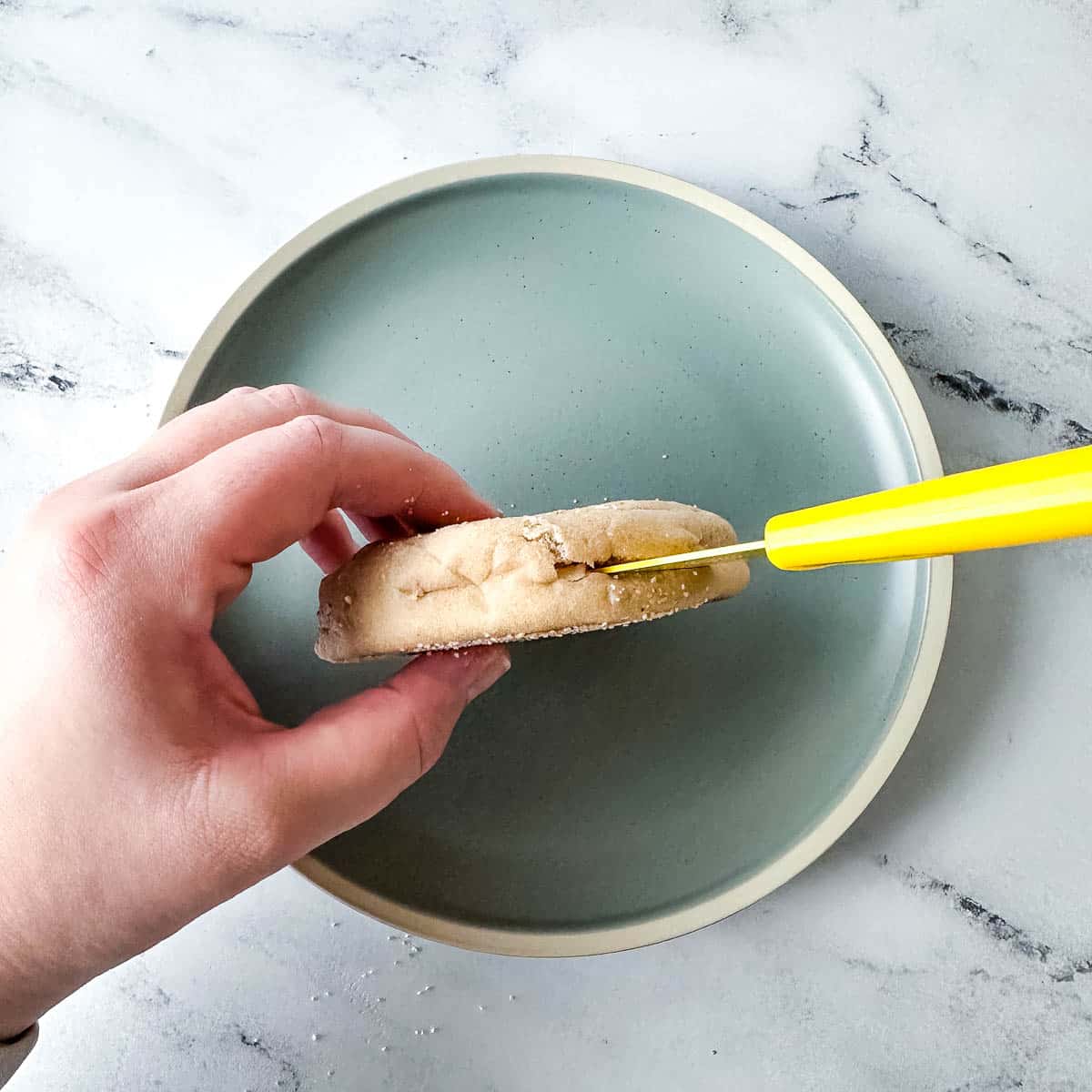 An English muffin is split with a yellow paring knife.