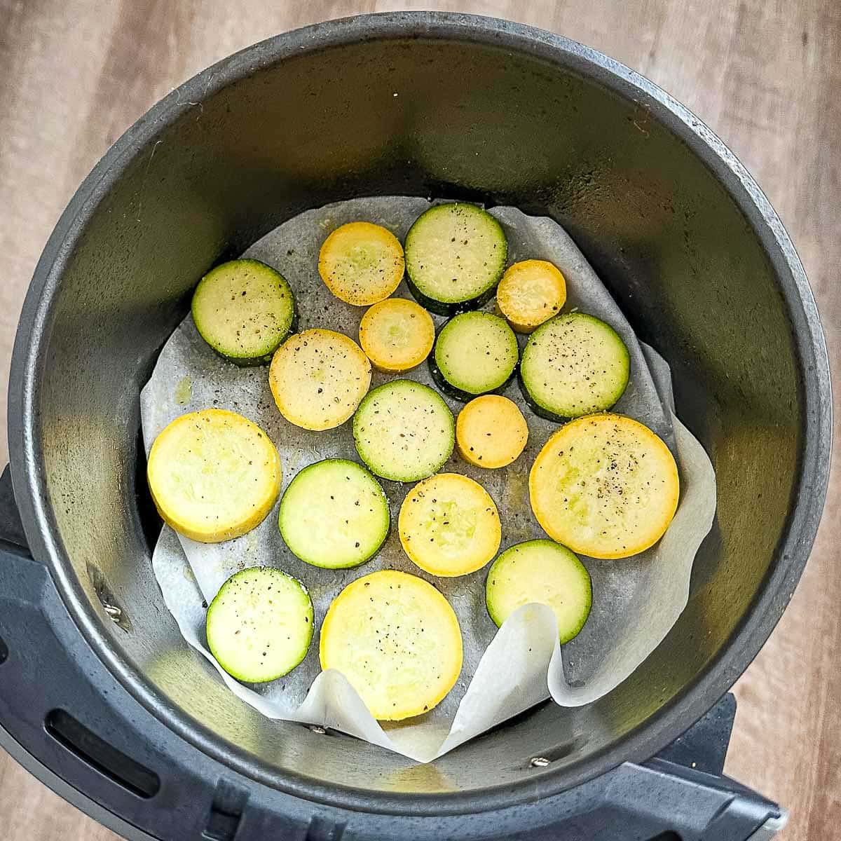 Zucchini and squash coated in olive oil, salt, and pepper in the air fryer basket.