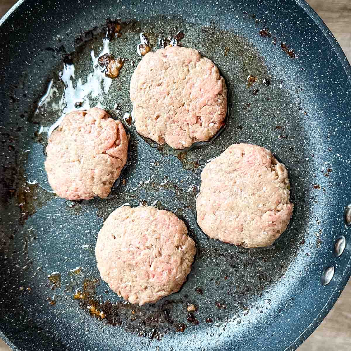 Raw turkey burger slider patties in a frying pan.