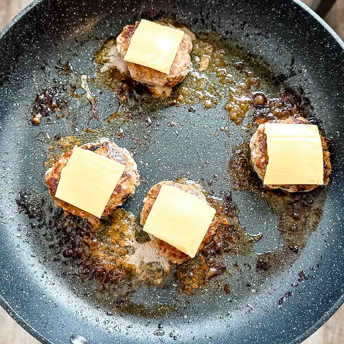 Turkey burger sliders topped with cheese in a frying pan.