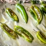 Roasted jalapenos on a foil-lined sheet tray.
