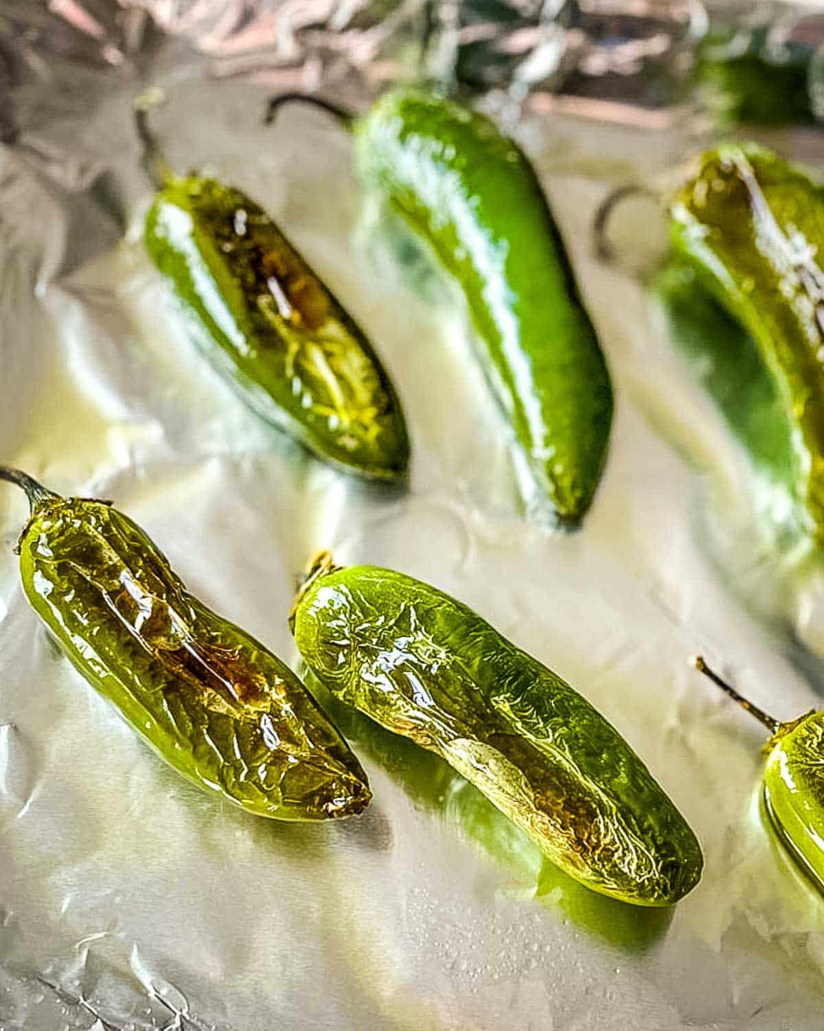 Roasted jalapenos on a foil-lined sheet tray.