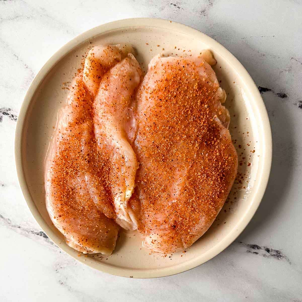 Two chicken breasts on a white plate coated liberally with Tajín seasoning.