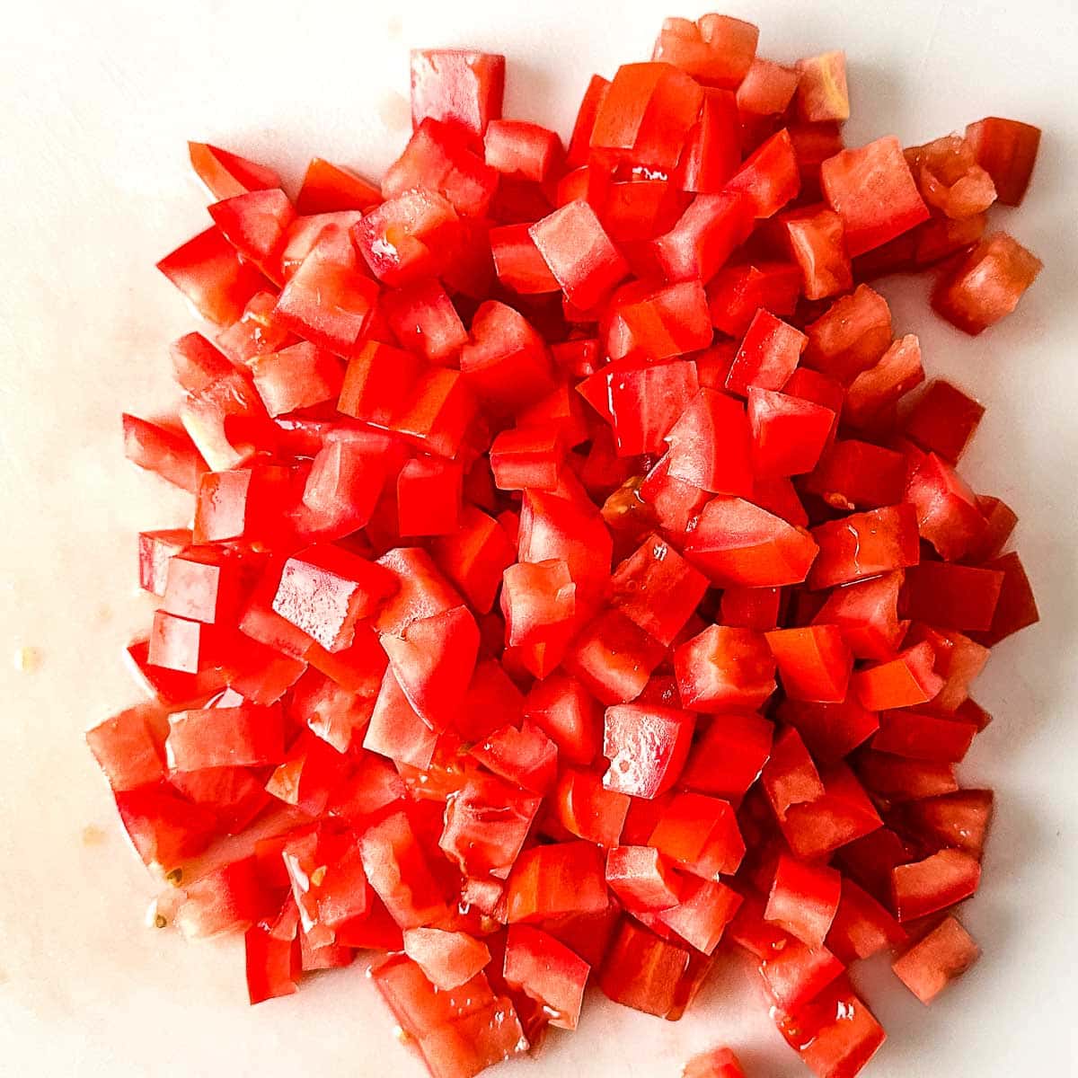 Diced tomato on a white cutting board.