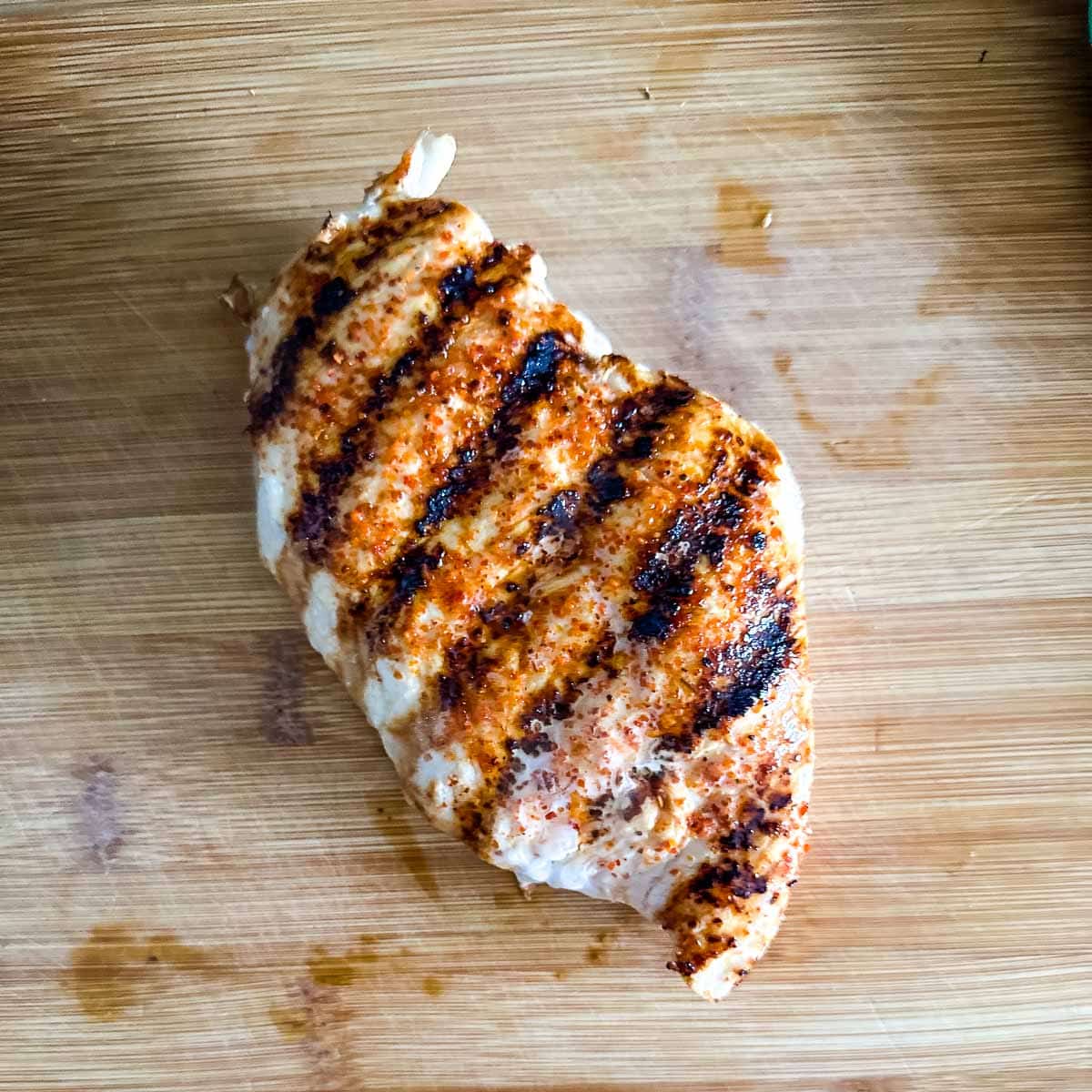 A Tajín Grilled Chicken breast sits on a wooden cutting board.