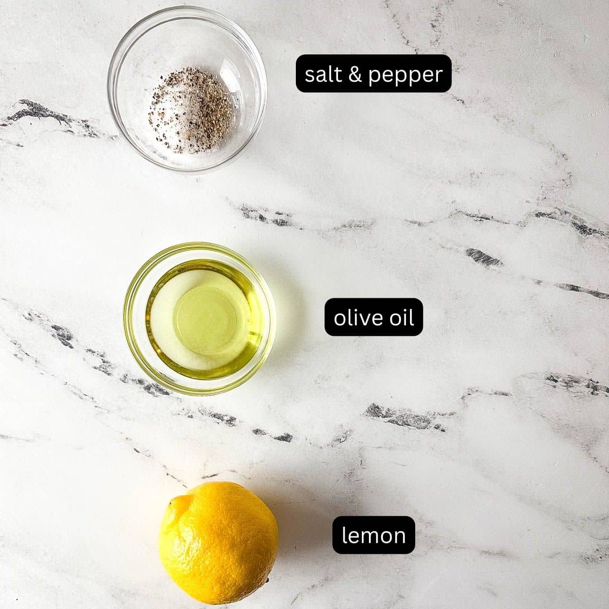 Labeled ingredients for lemon vinaigrette on a white marble counter.