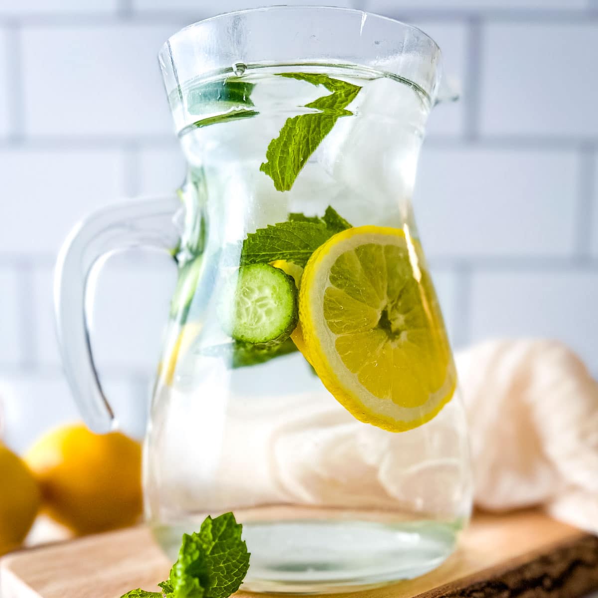 Cucumber lemon mint water in a clear pitcher on a rustic wooden cutting board.
