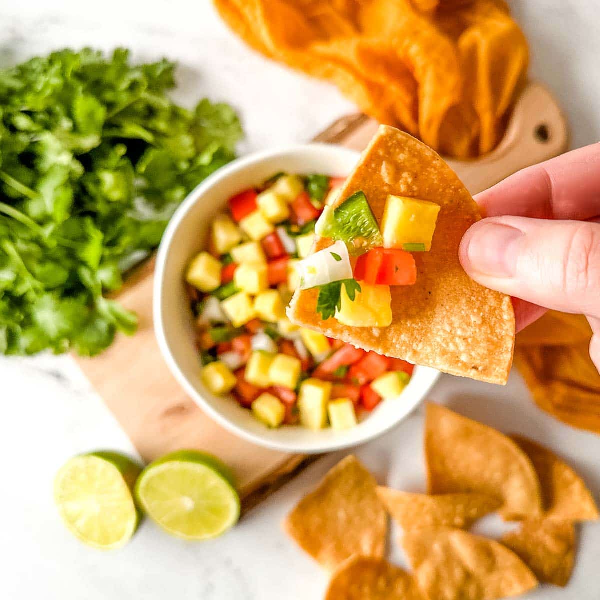Overhead shot of a chip with pineapple salsa on it over a bowl of pineapple pico de gallo in a white bowl.