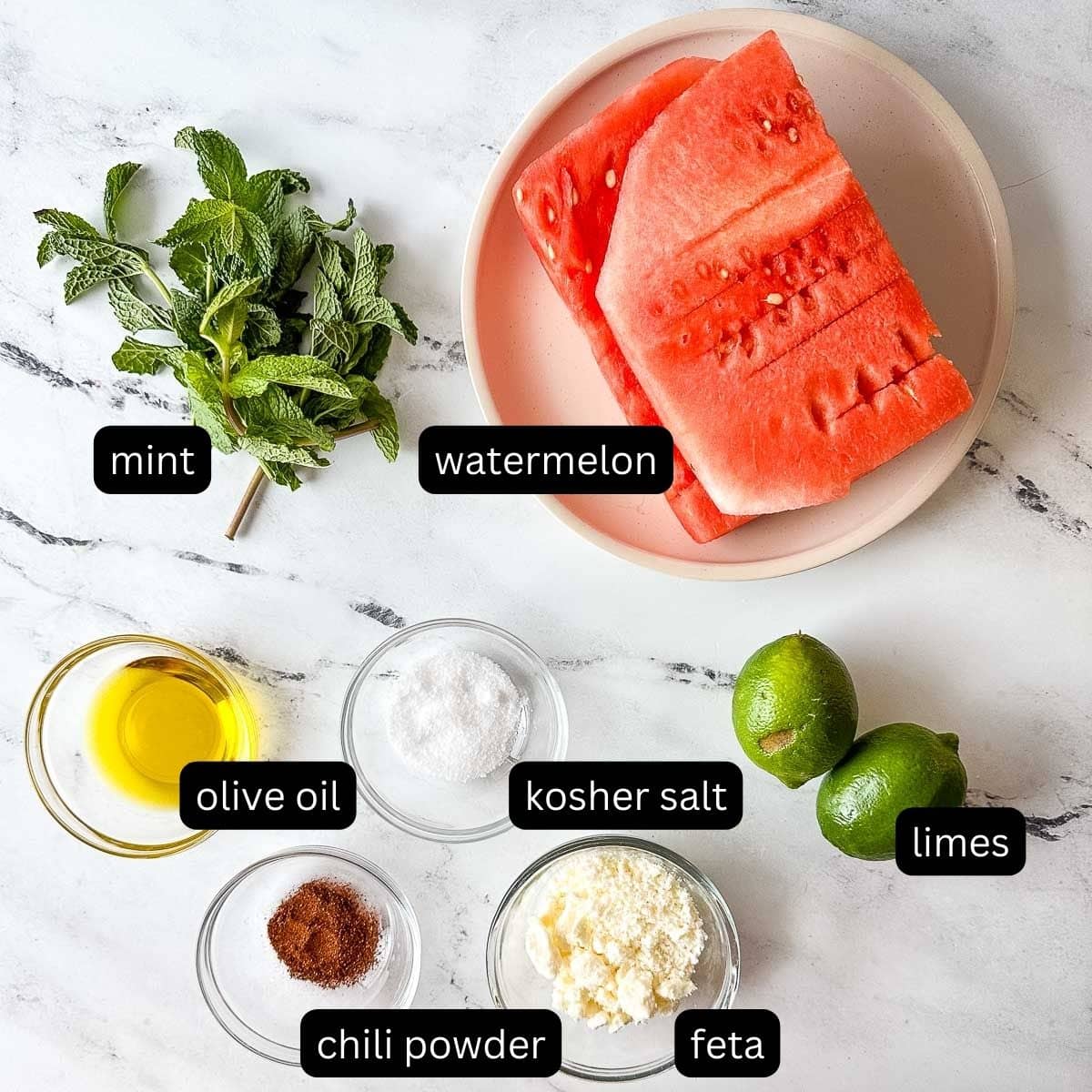 Labeled ingredients for watermelon mojito salad on a white counter.