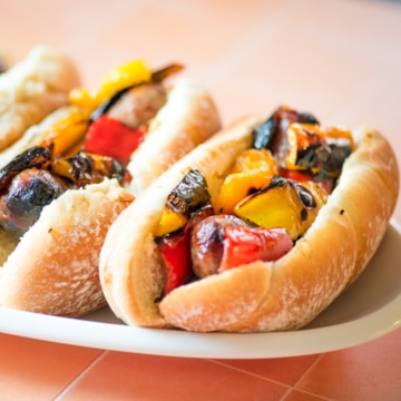 Closeup side view shot of sausage and peppers sandwiches on a white platter.