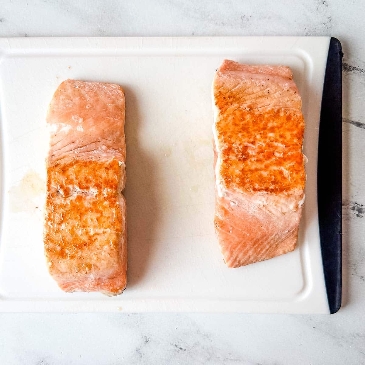 Two cooked salmon fillets on a white cutting board.