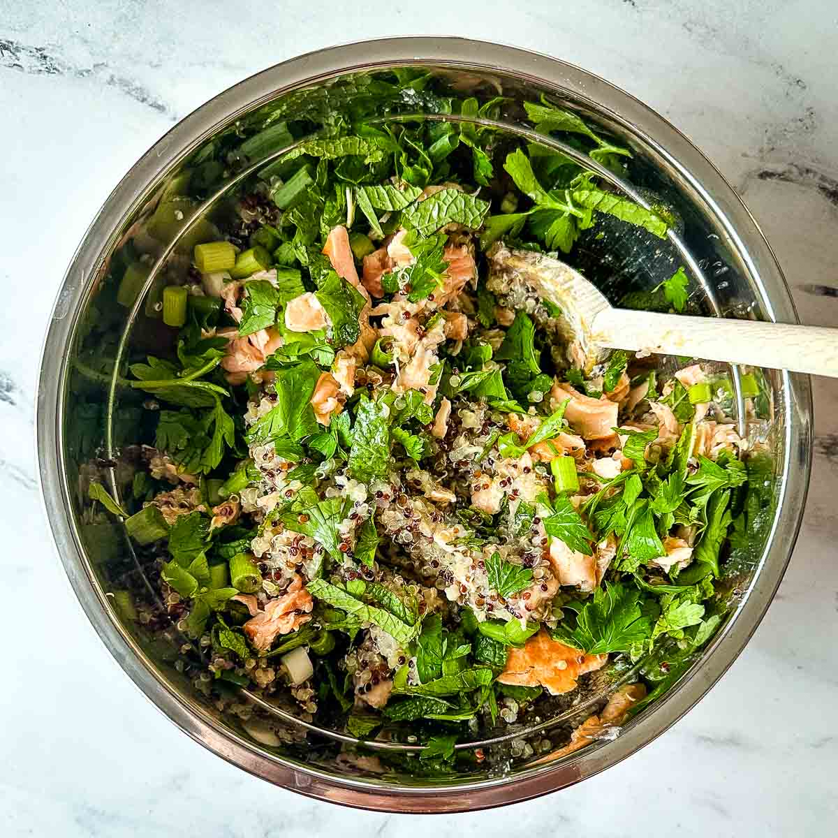 The ingredients for salmon quinoa salad are mixed together in a silver bowl.