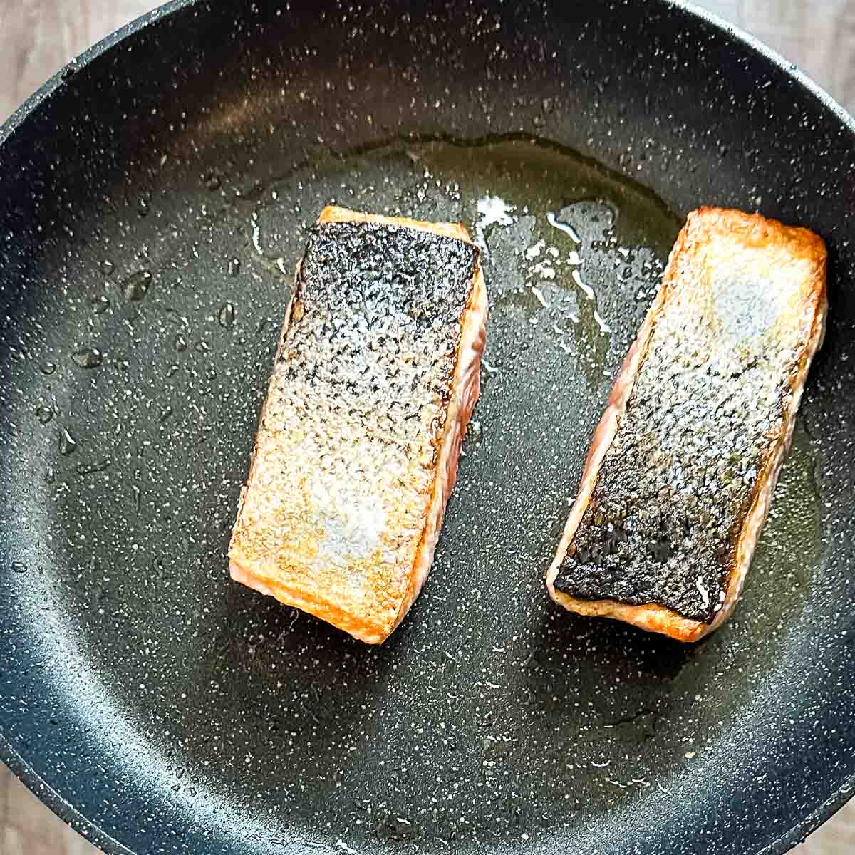 Salmon fillets are cooked skin-side up in a frying pan.