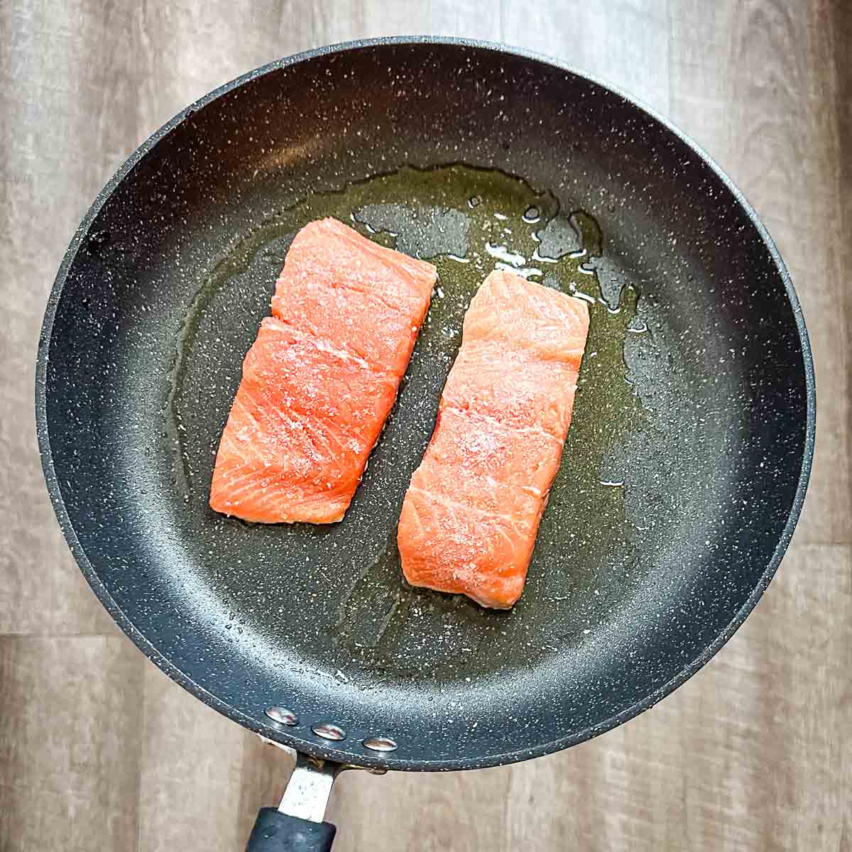 Two skin-side down salmon fillets cooking in a frying pan.