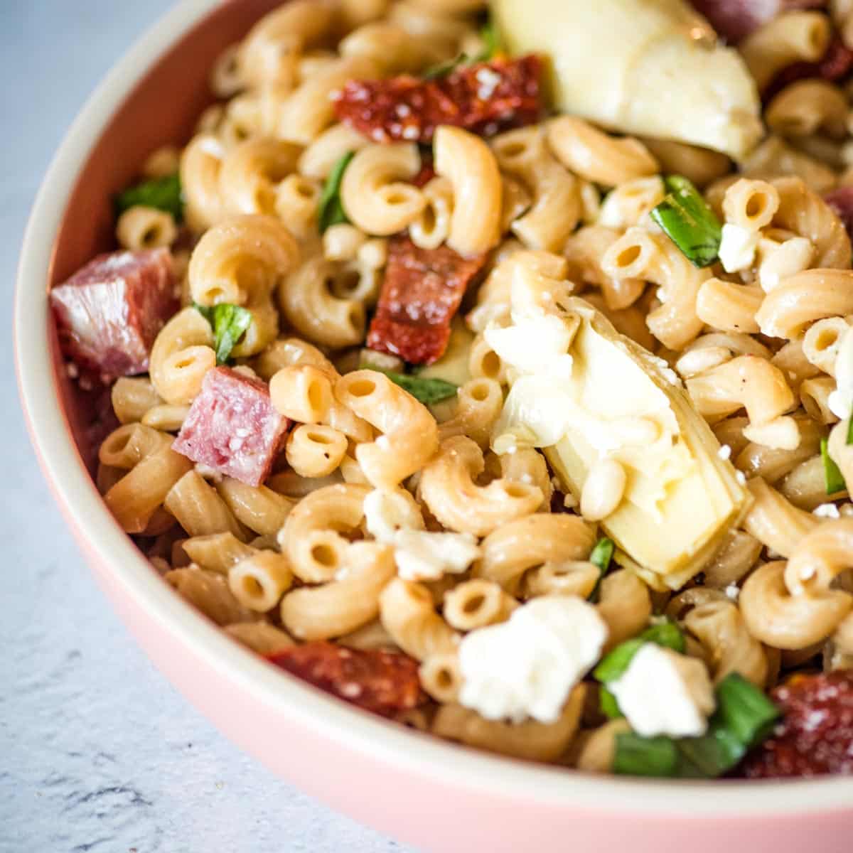 Closeup shot of whole wheat pasta salad in a pink dish.