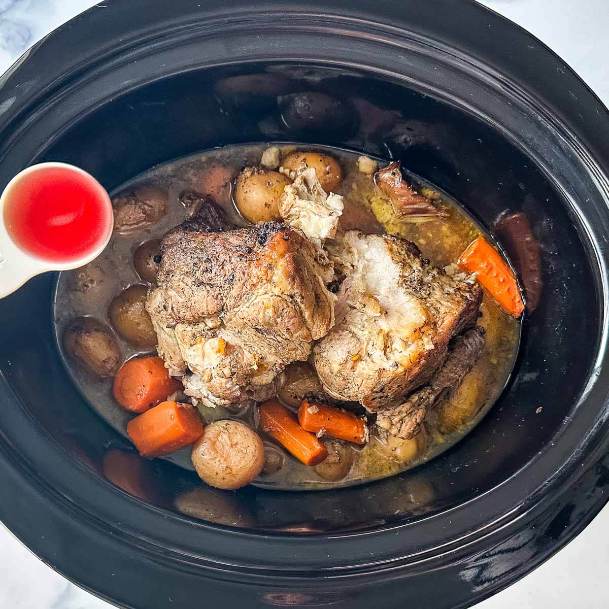 Red wine vinegar is added to a crock pot full of pork and vegetables.