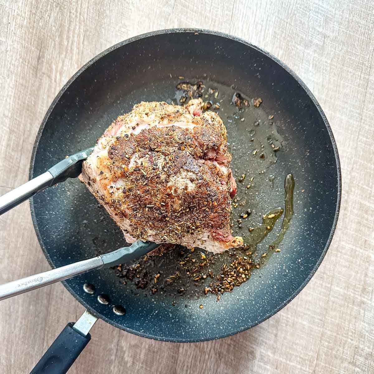 A pork roast is browned in a frying pan.