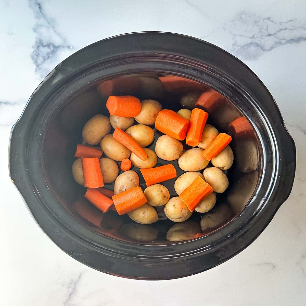 A crock pot filled with carrots and potatoes.