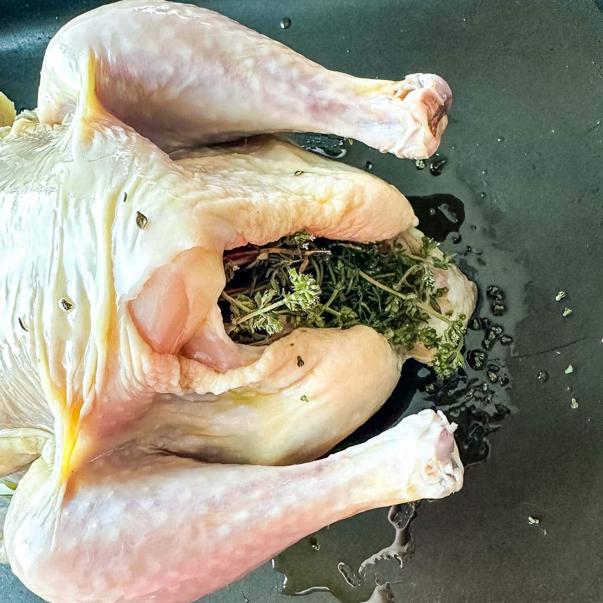 A chicken in a pan with thyme in the cavity.