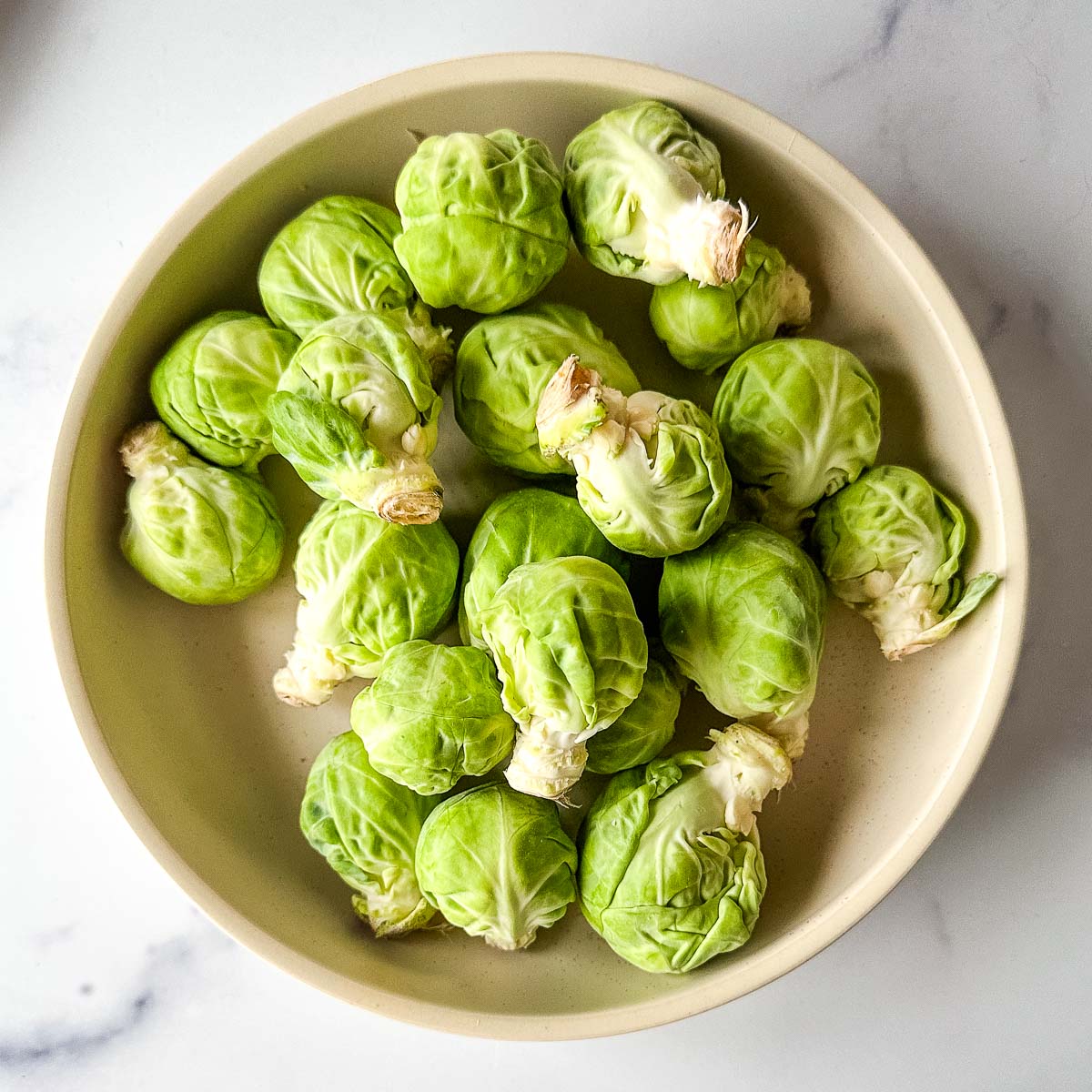 Brussels sprouts in a bowl on a marble counter.