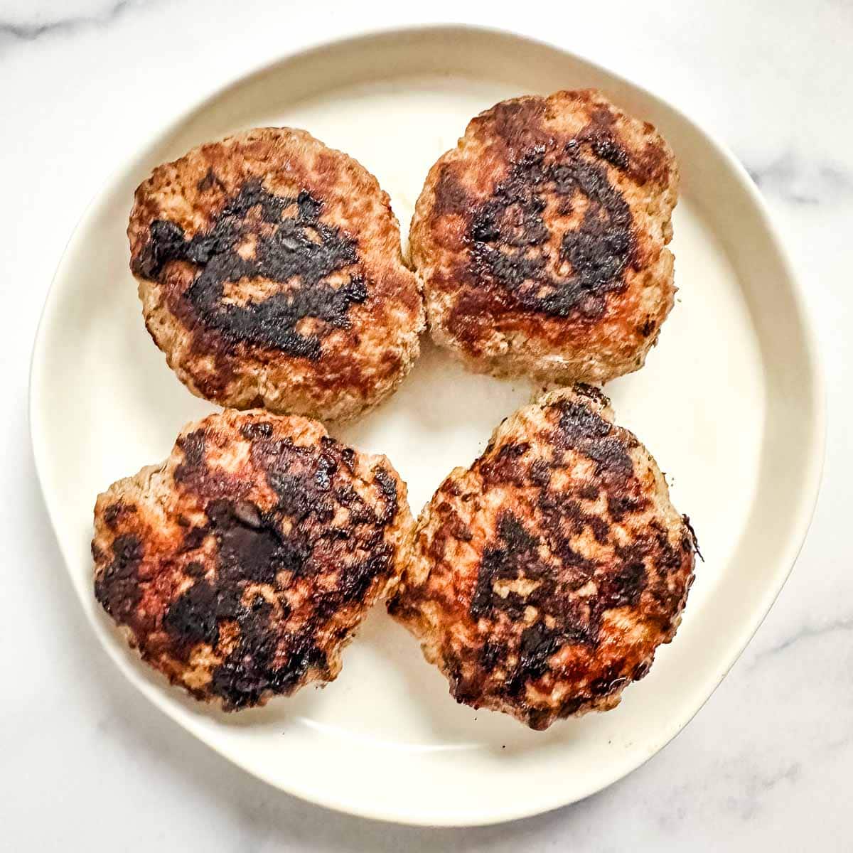Four cooked turkey burger patties on a white plate.