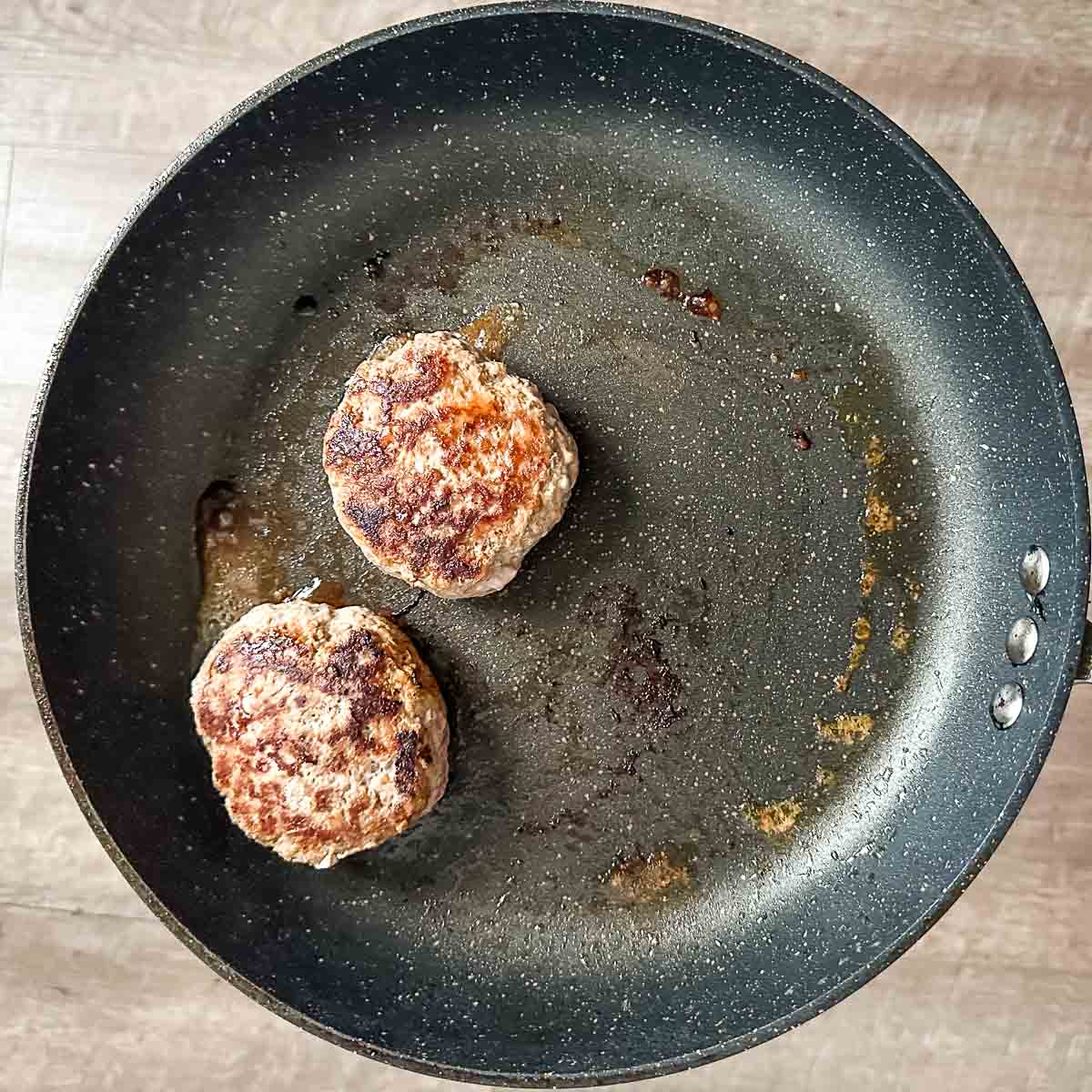Two cooked turkey burger patties in a pan.