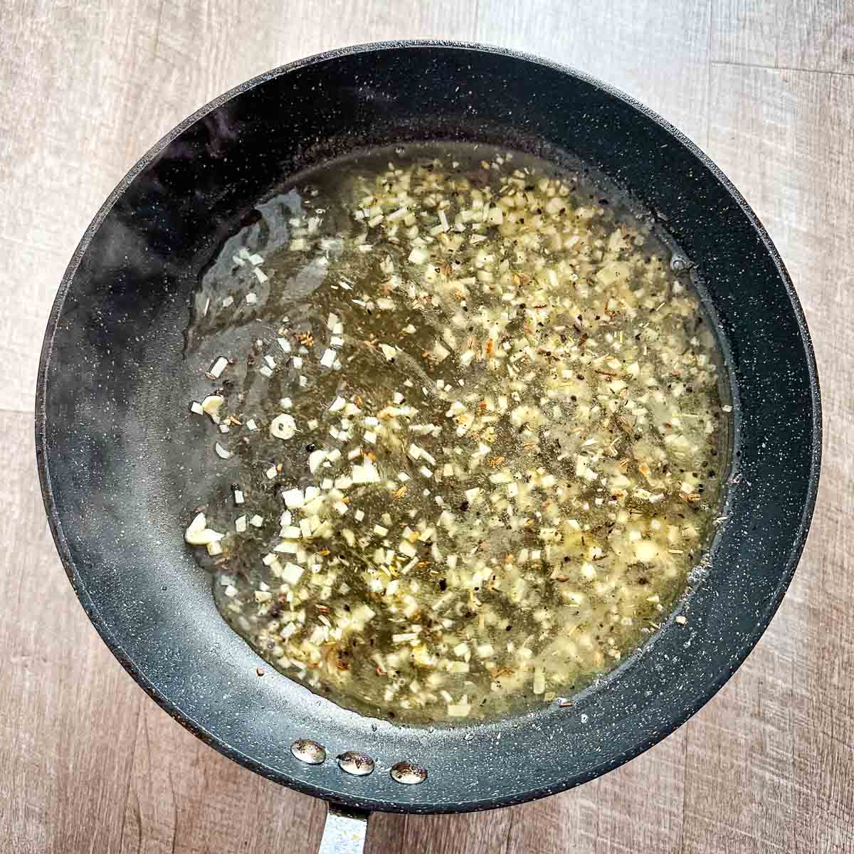 A frying pan filled with garlic, white wine, and chicken stock.