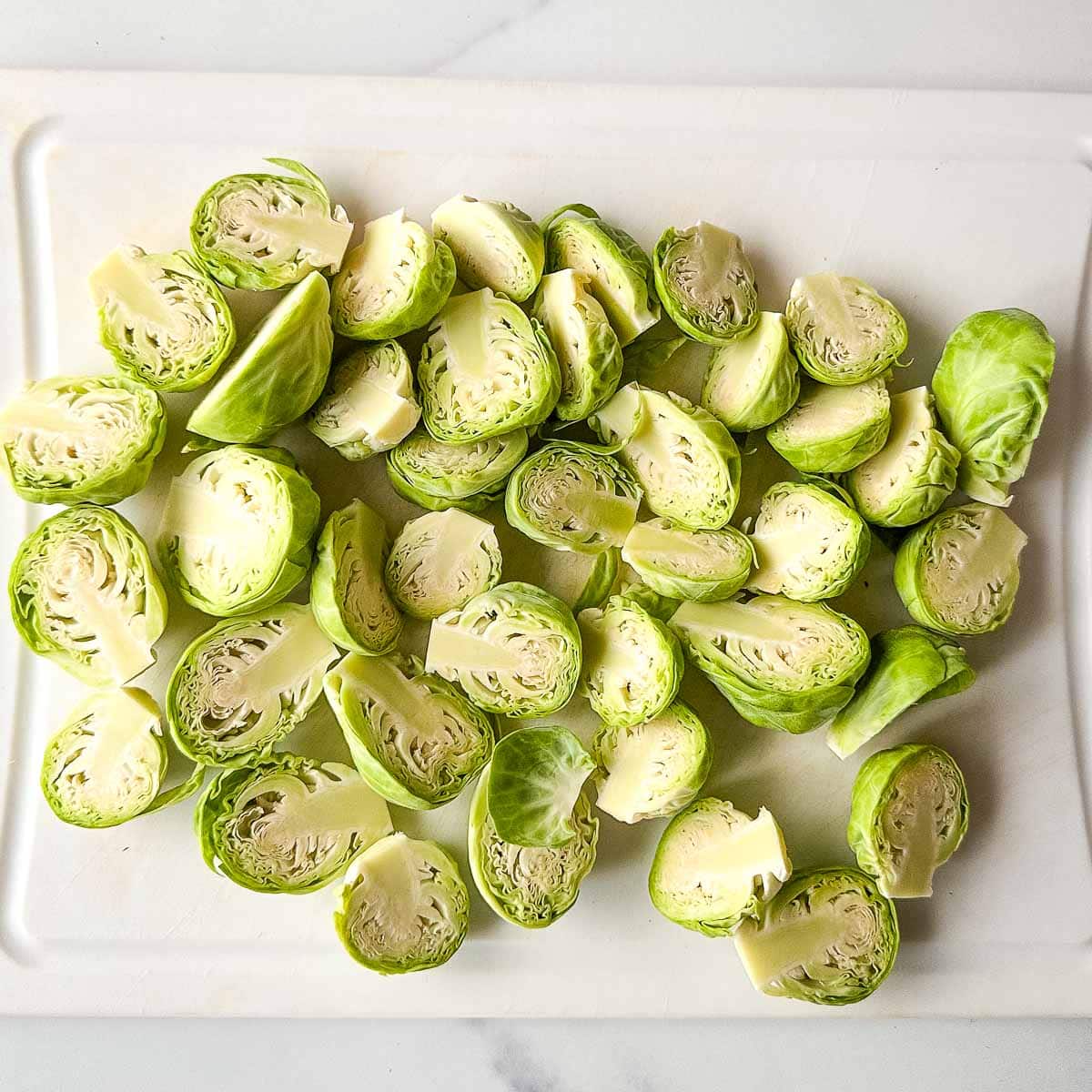 Brussels sprouts on a white cutting board.