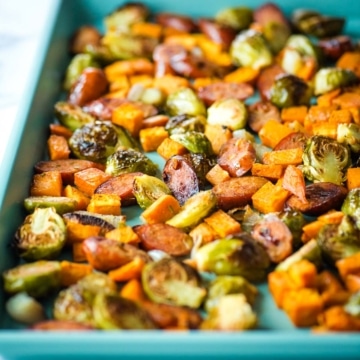 Roasted brussels sprouts, sweet potatoes, shallots, and chicken sausage on a baking sheet.