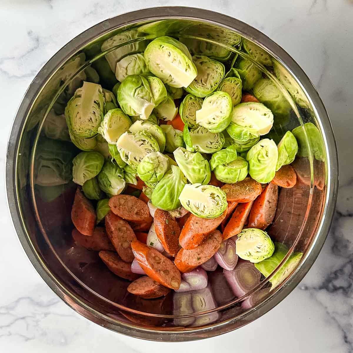 Brussels sprouts, sweet potatoes, shallots, and sausage in a metal bowl.
