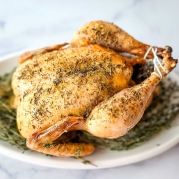 A roasted chicken with herbs on a white plate.