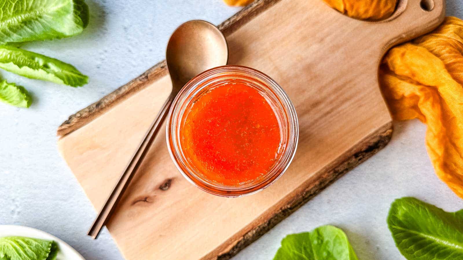A jar of hot harissa vinaigrette on a wooden cutting board.