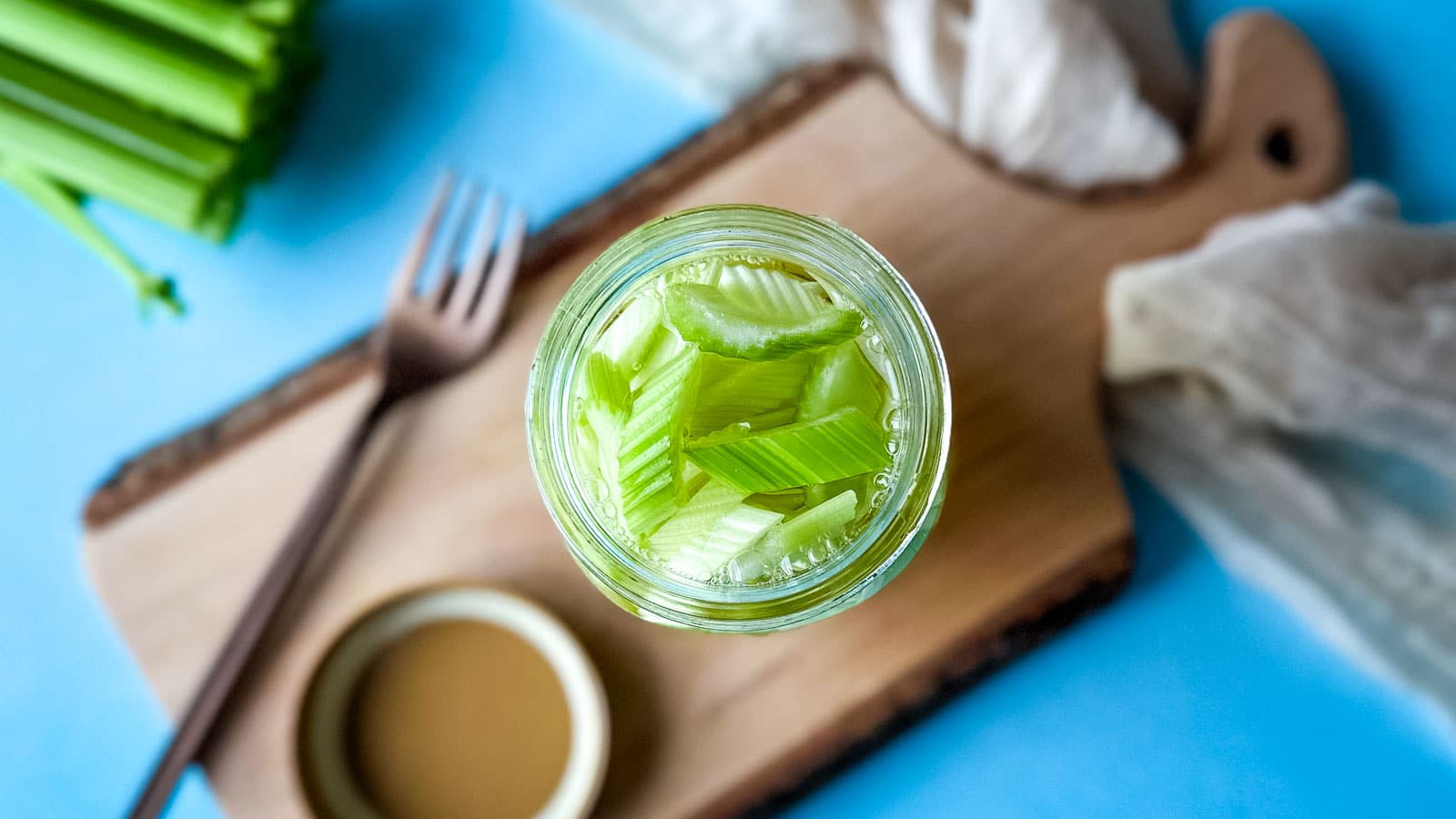 A jar of pickled celery on a cutting board with a fork.