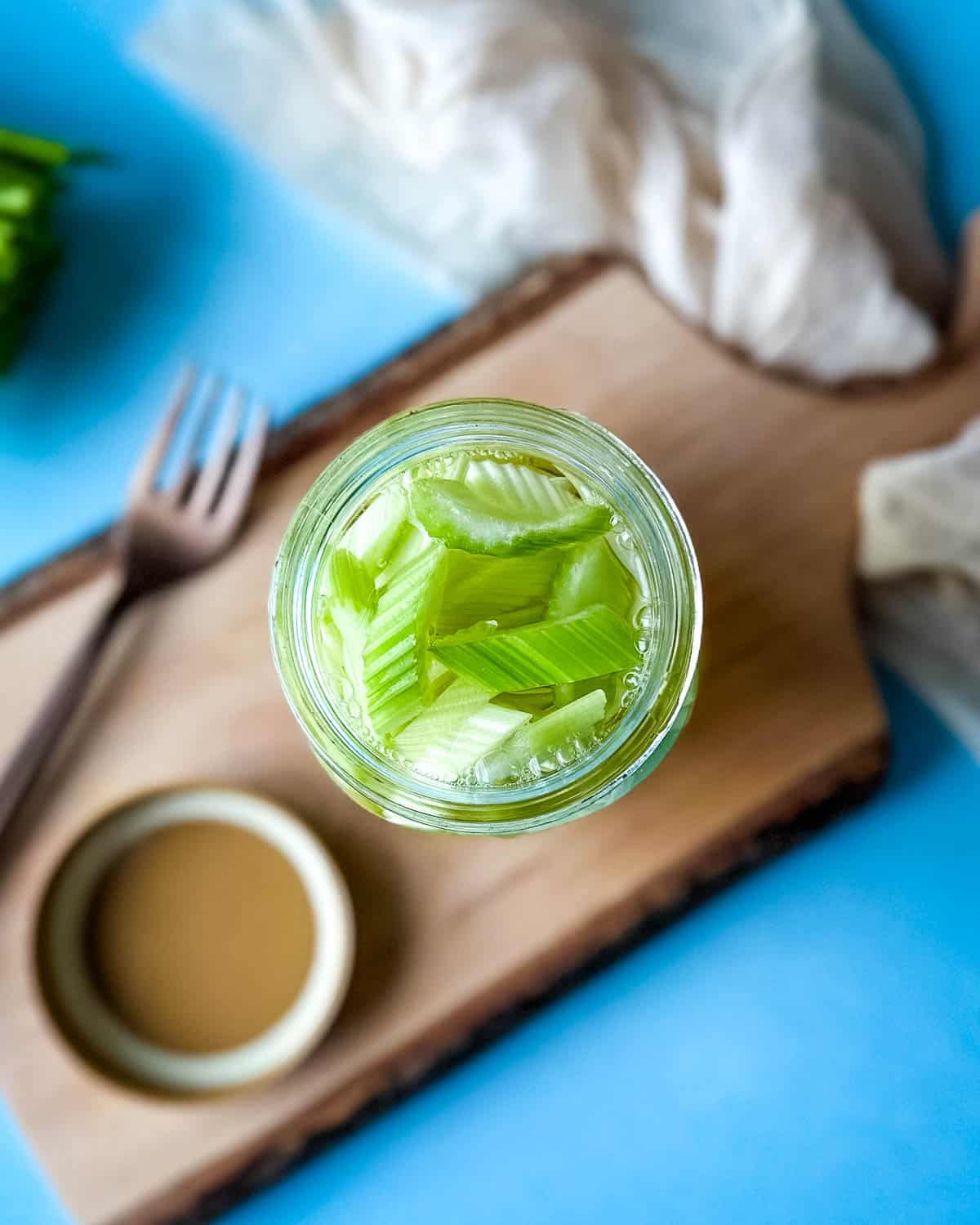 A jar of pickled celery on a wooden cutting board.