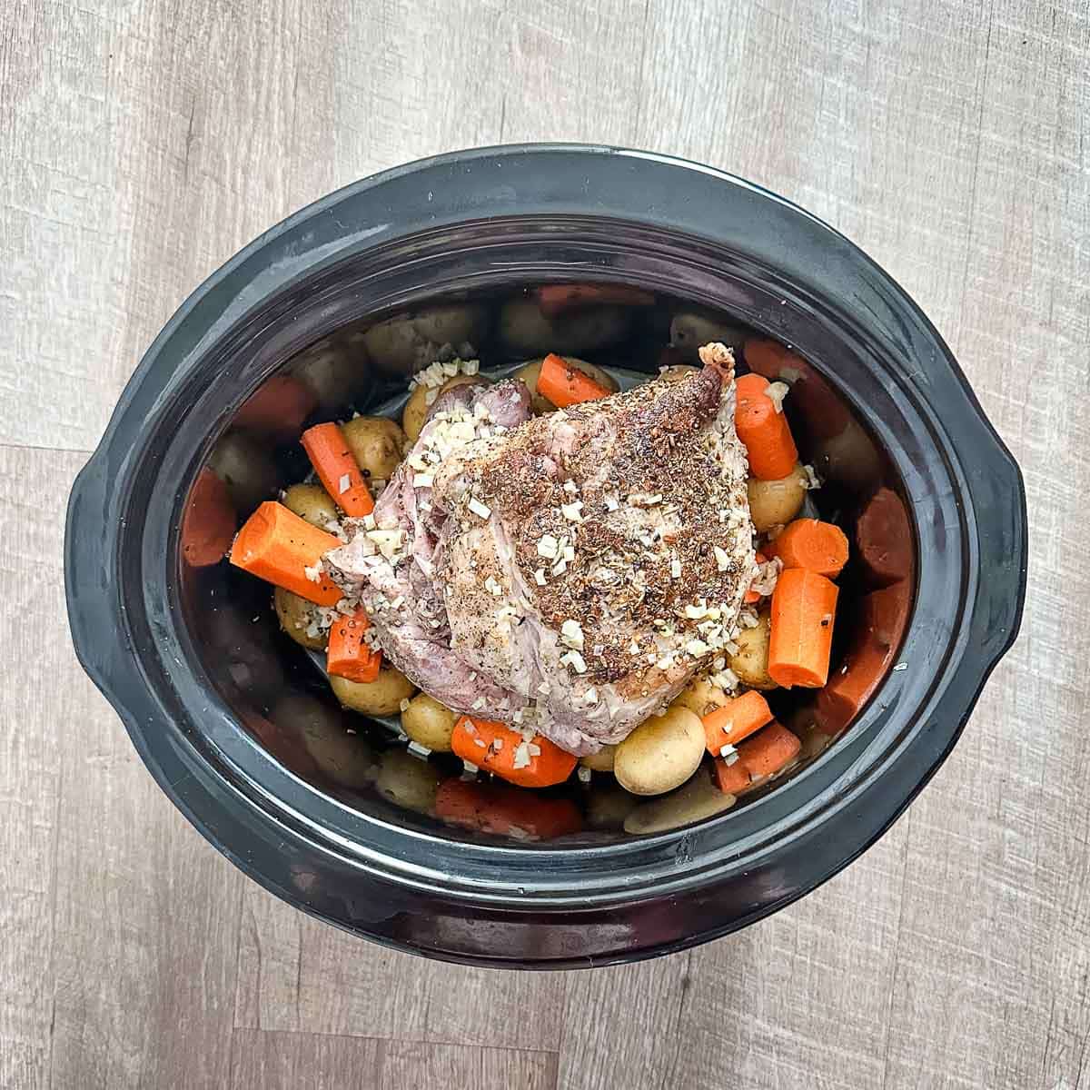A crock pot full of pork roast, potatoes, carrots, and cooking liquid.