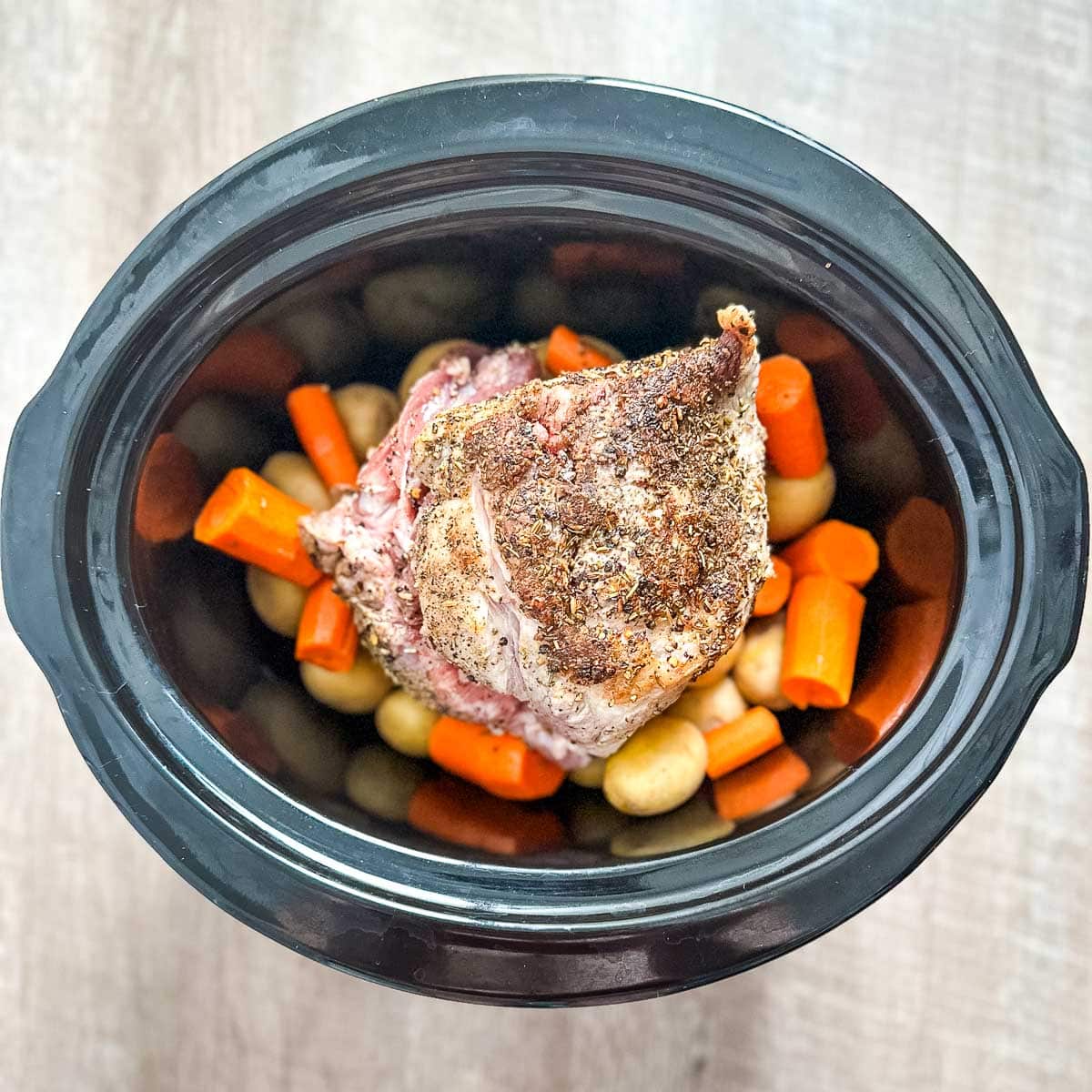 A crock pot filled with pork roast, potatoes, and carrots.