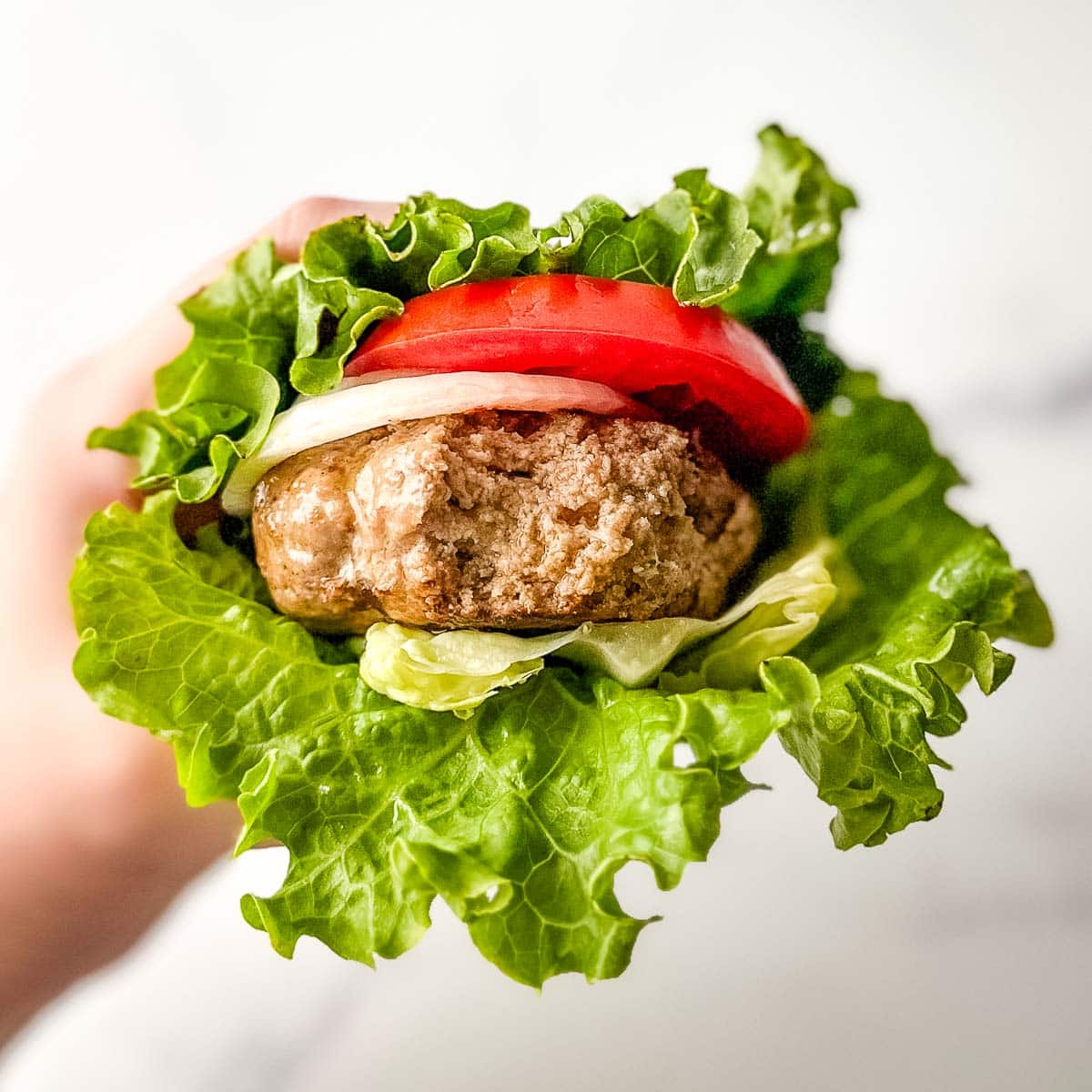 A hand holding up a turkey burger lettuce wrap.
