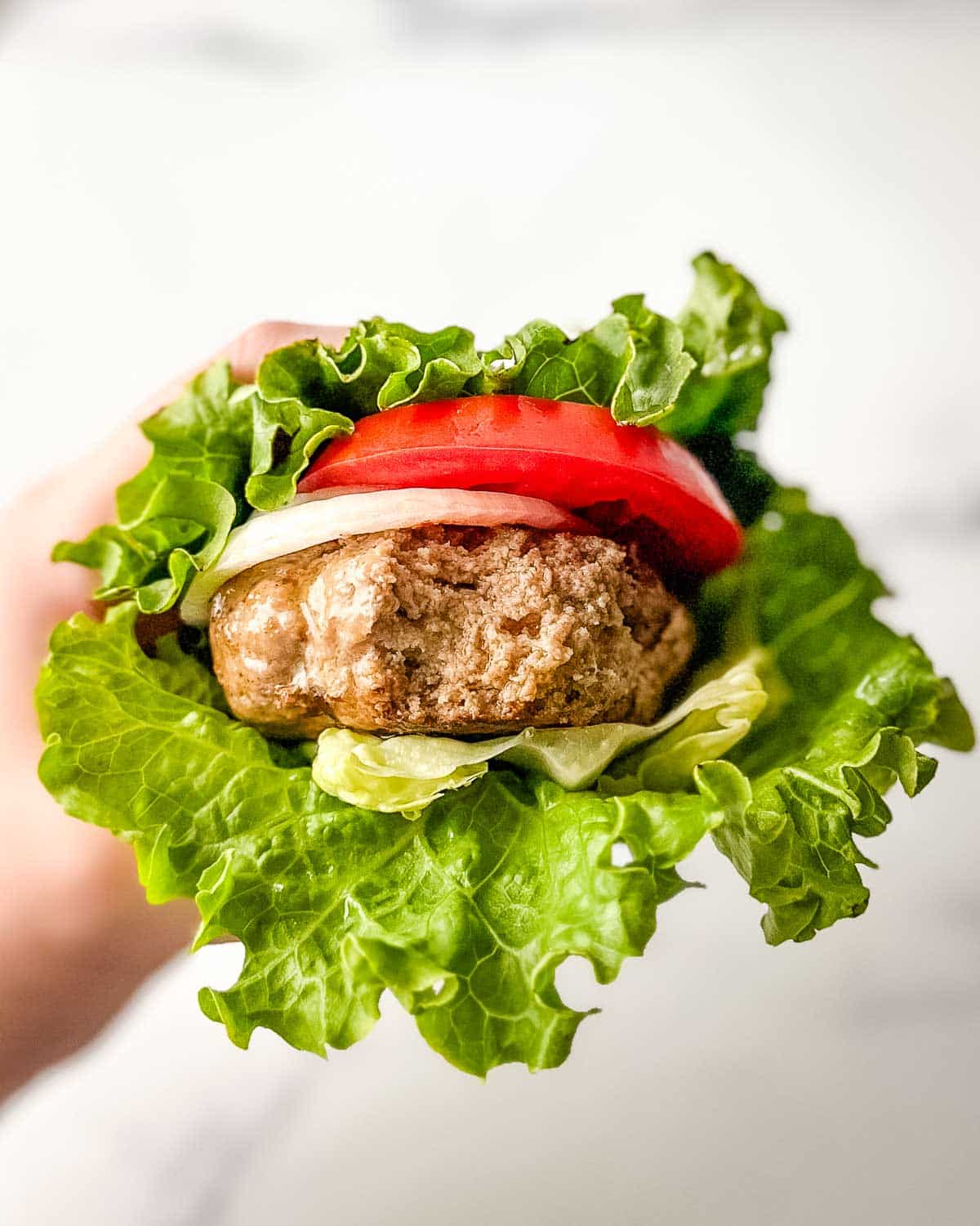 A person holding up a turkey burger lettuce wrap.