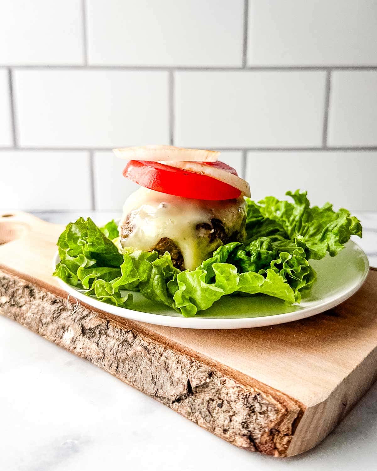 A turkey burger lettuce wrap with melted cheese, tomato and onion on a plate.