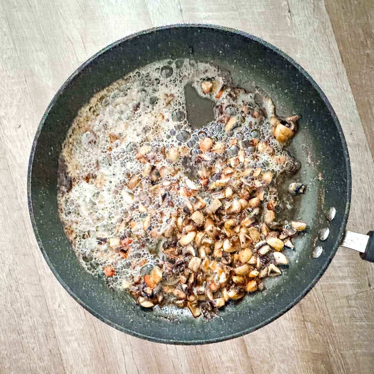 A frying pan with mushrooms and butter in it.