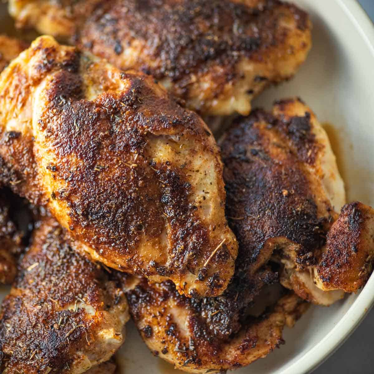Blackened chicken thighs in a white bowl.