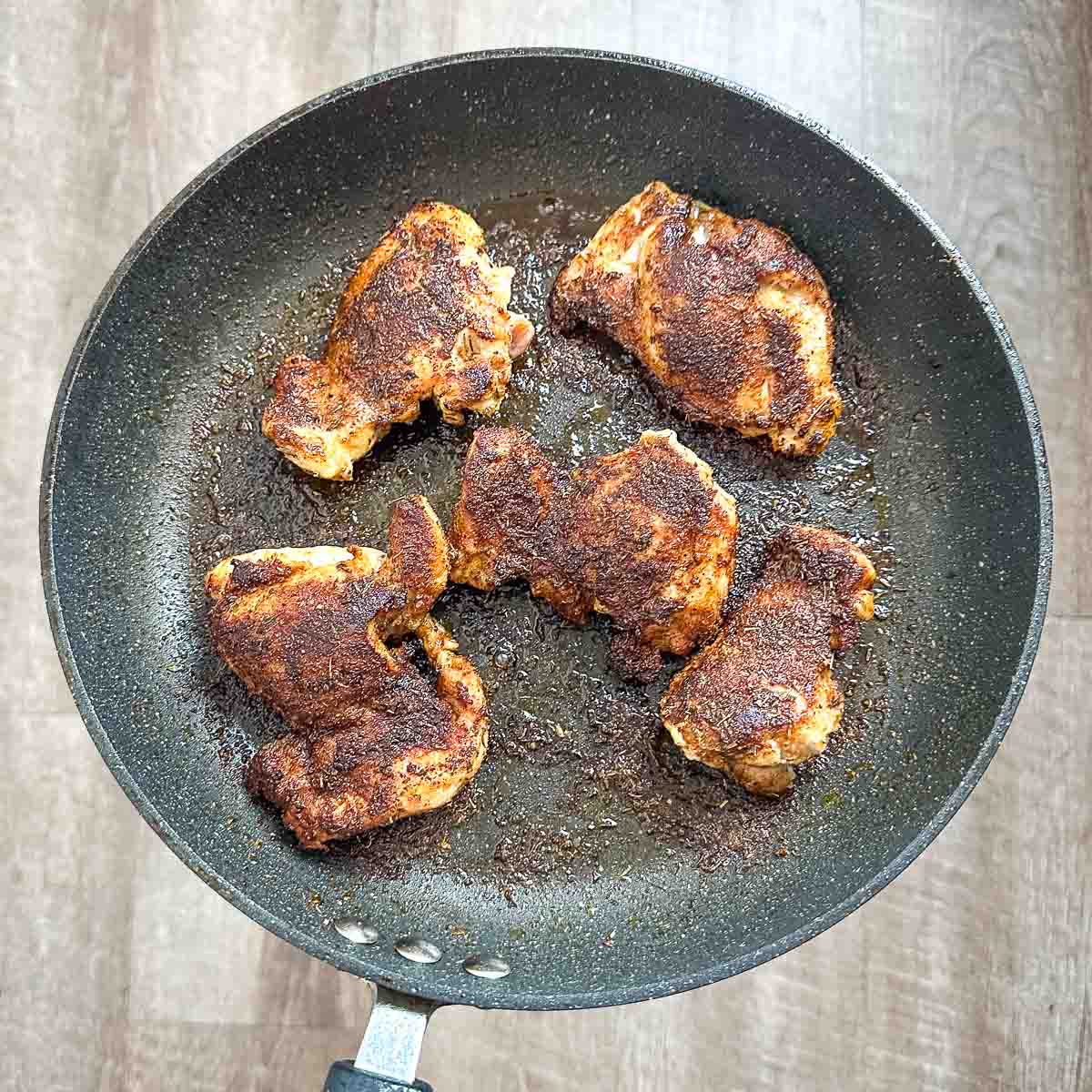 A frying pan with cooked blackened chicken thighs in it.