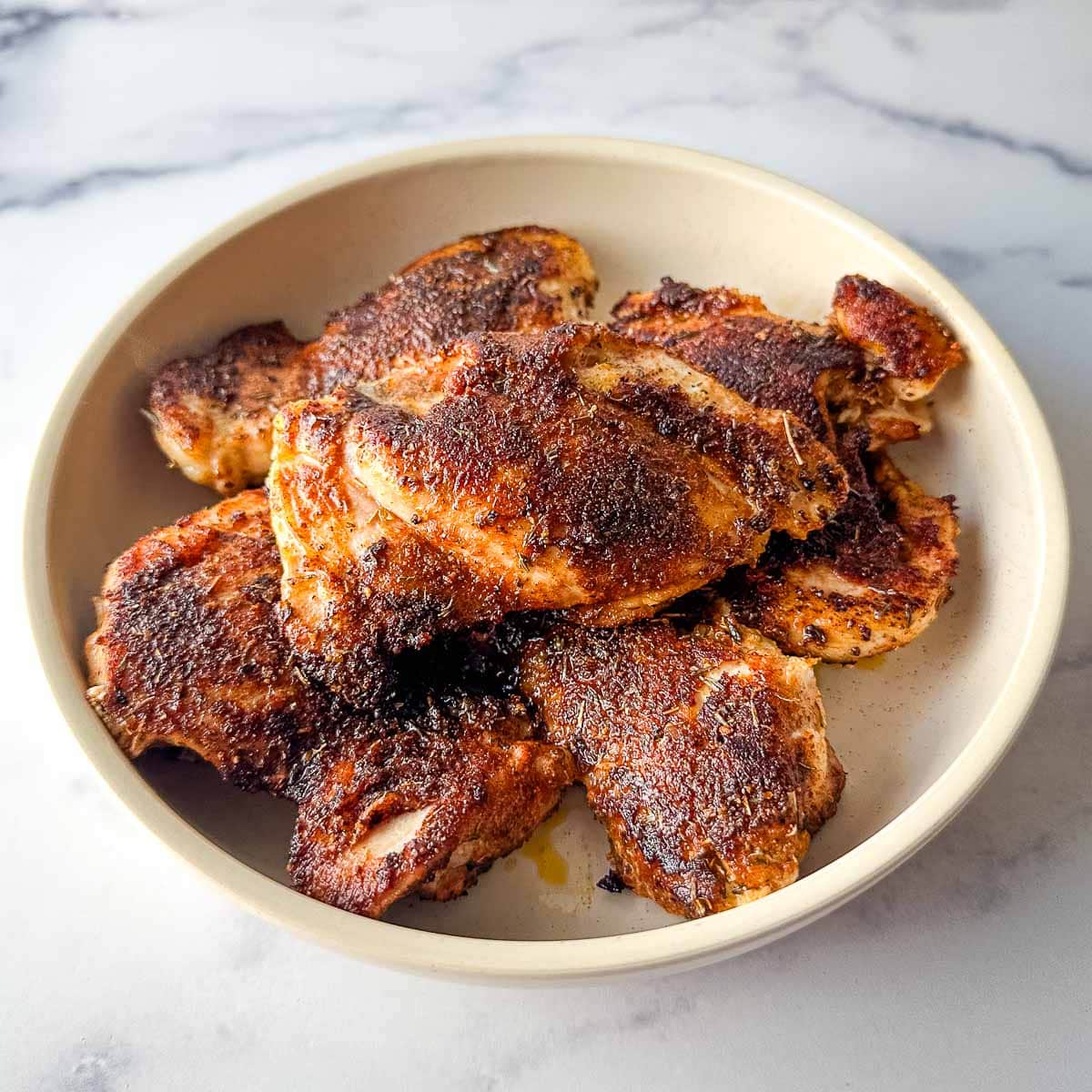 Blackened chicken thighs in a bowl on a marble table.