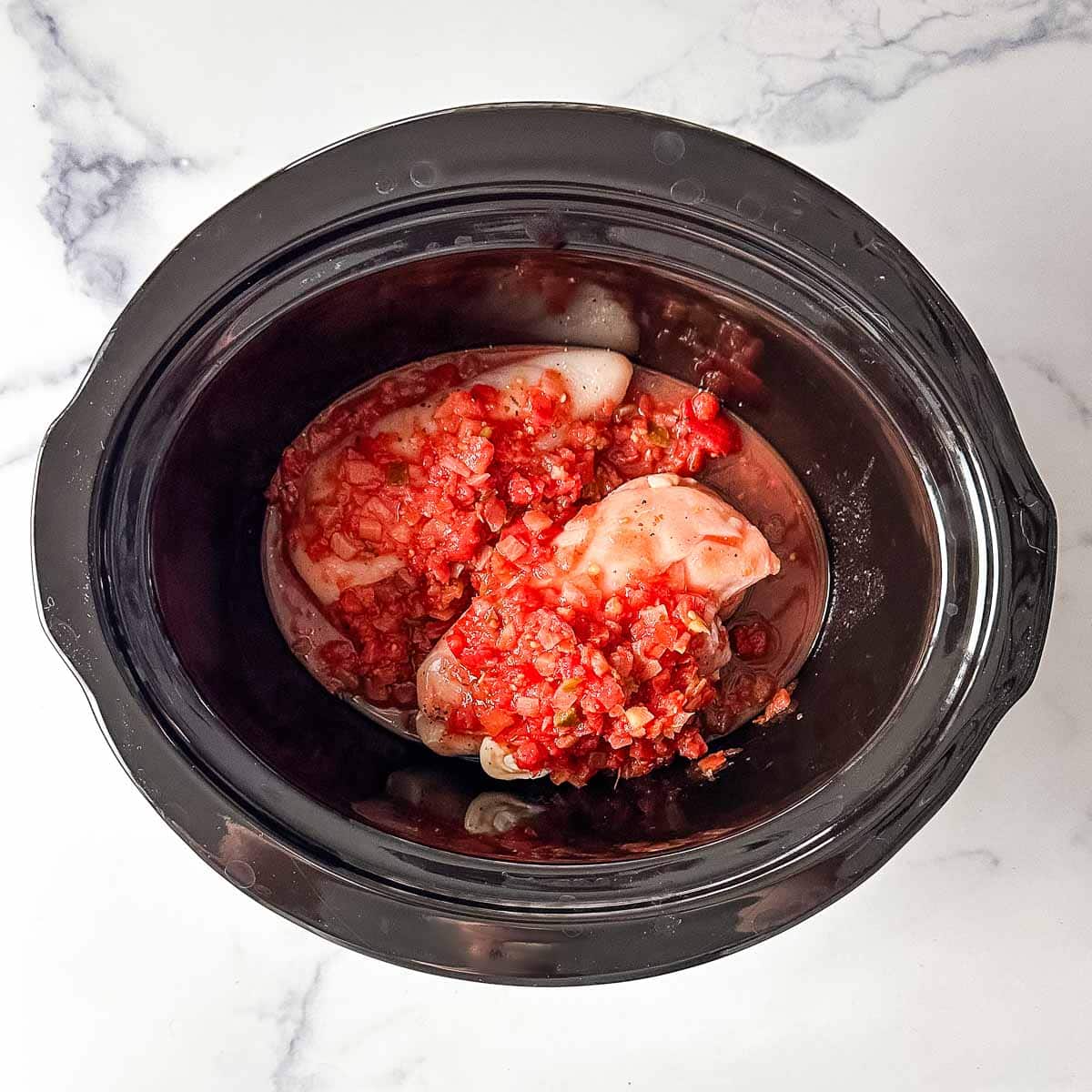 A crock pot filled with chicken and salsa.