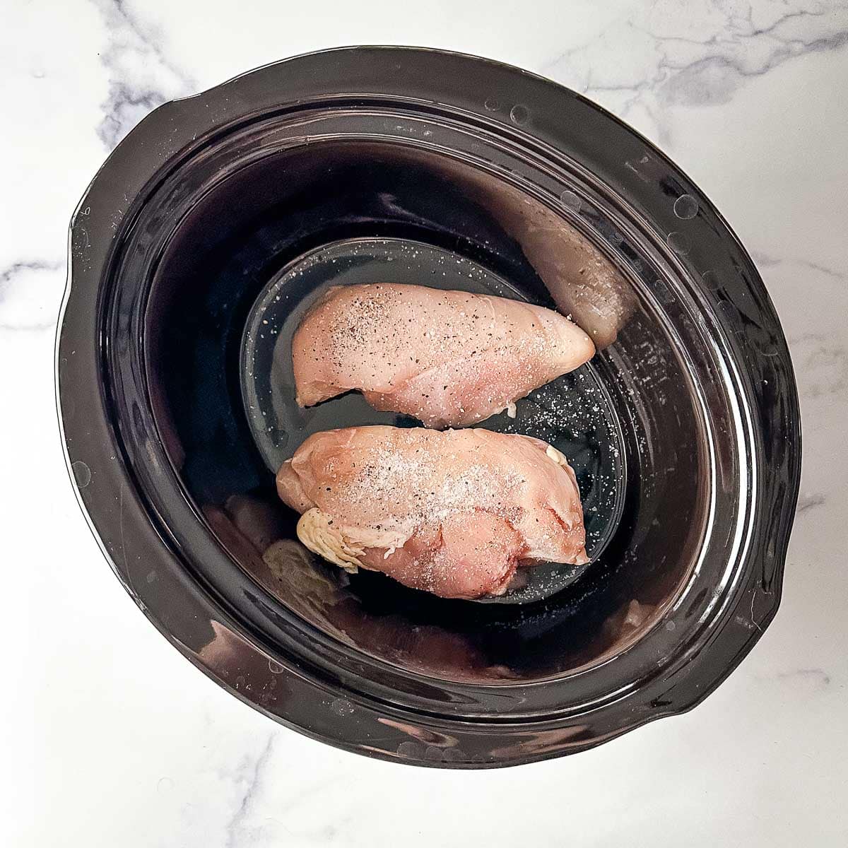A black crock pot with chicken in it.