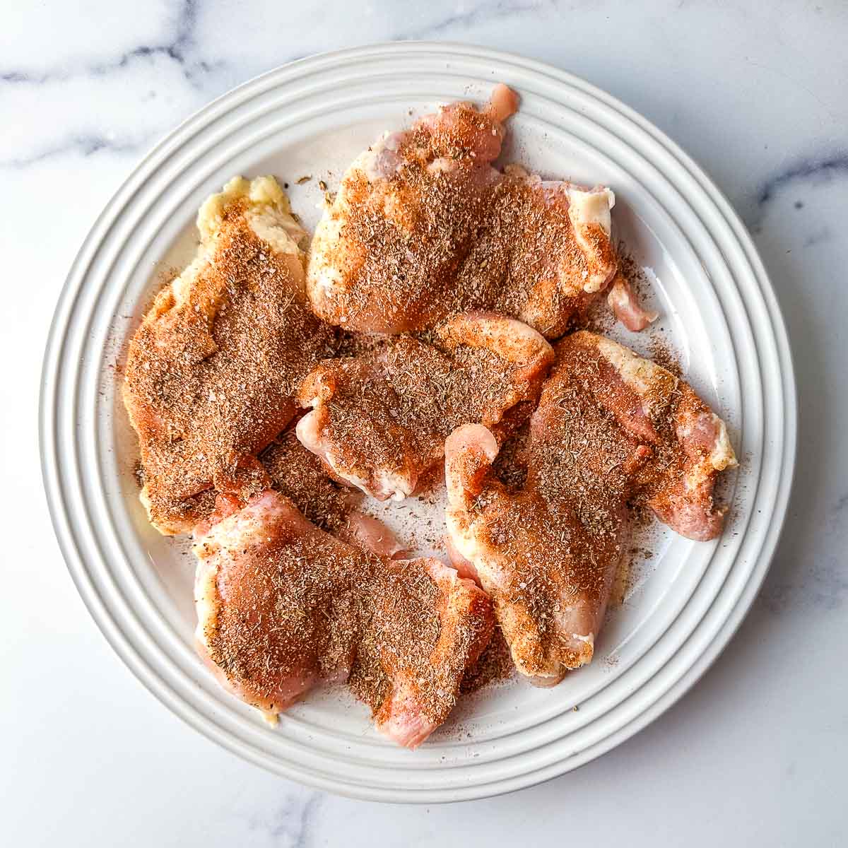 Seasoned chicken thighs on a white plate.