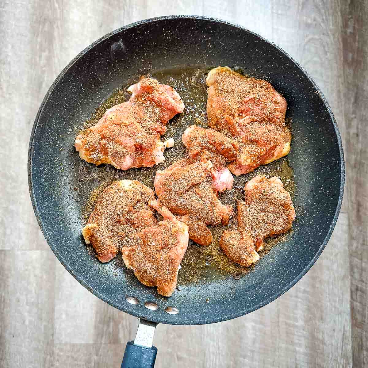 A frying pan with blackened chicken thighs in it.
