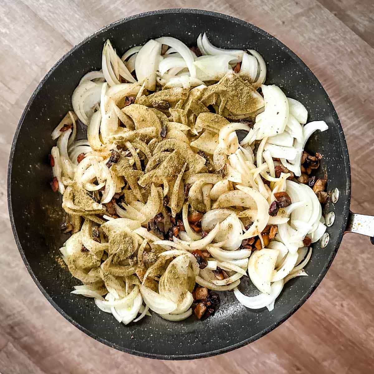 Onion, mushroom, and poultry seasoning in a frying pan.