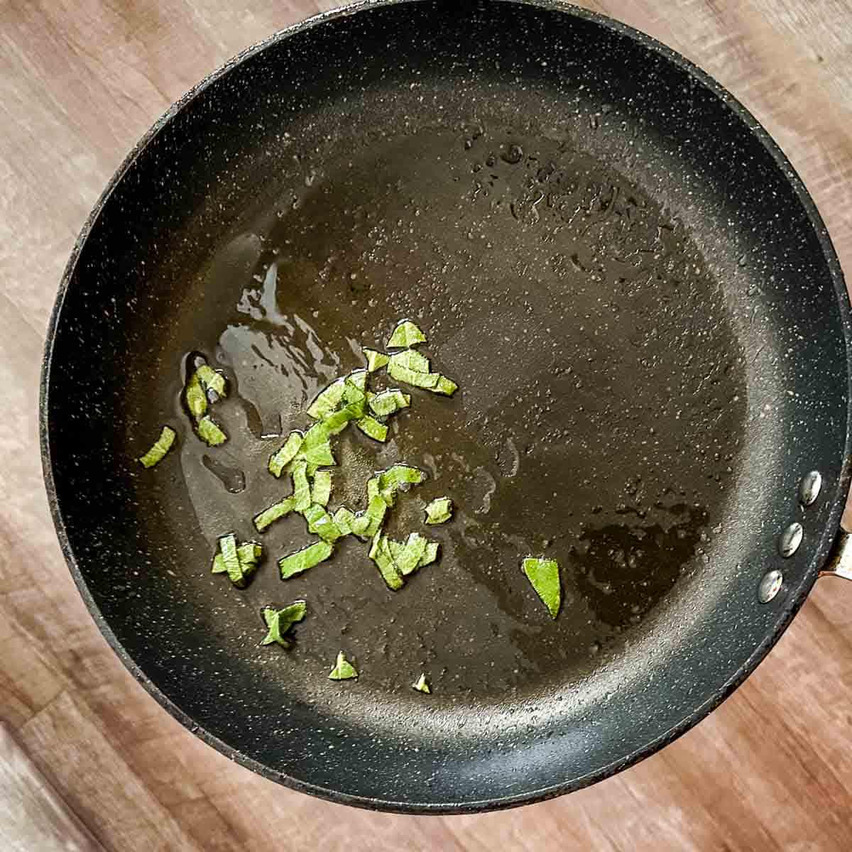 A frying pan with sliced sage in it.