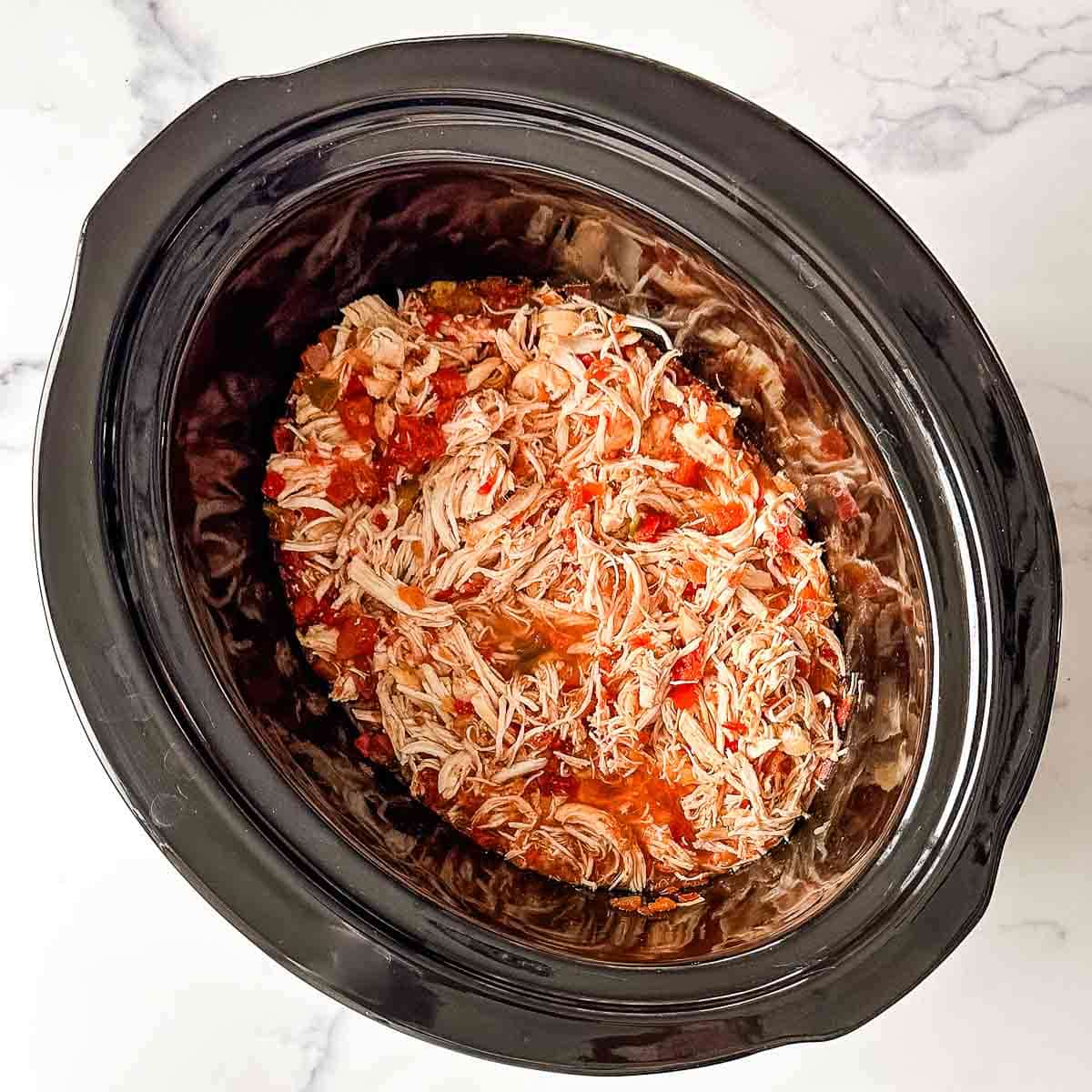 A crock pot filled with shredded chicken and salsa.